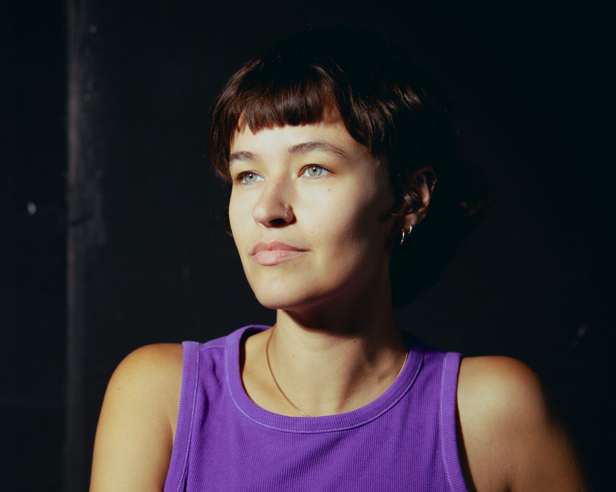 Porträt von Alma Akaya im lila Top, sie schaut in warmem Licht zur Seite