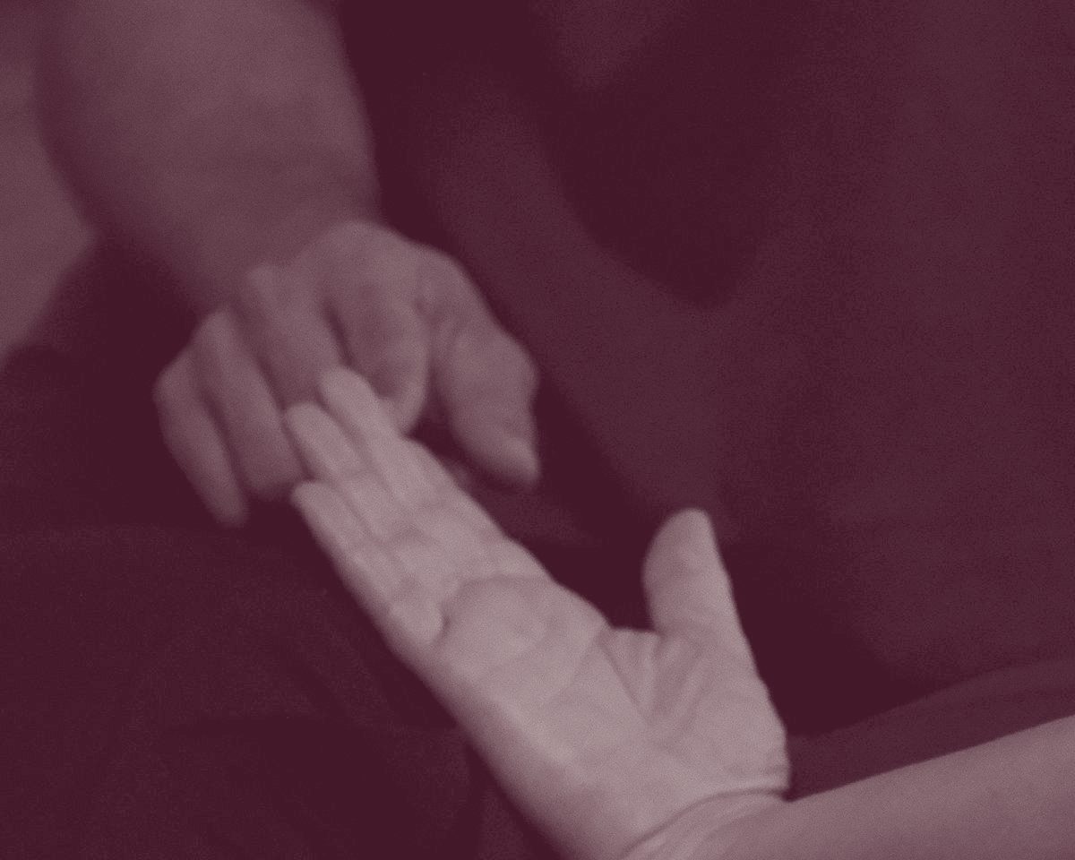Zwei Hände in warmem Licht vor dunklem Hintergrund, eine offene Handfläche, die andere Hand reicht zu ihr